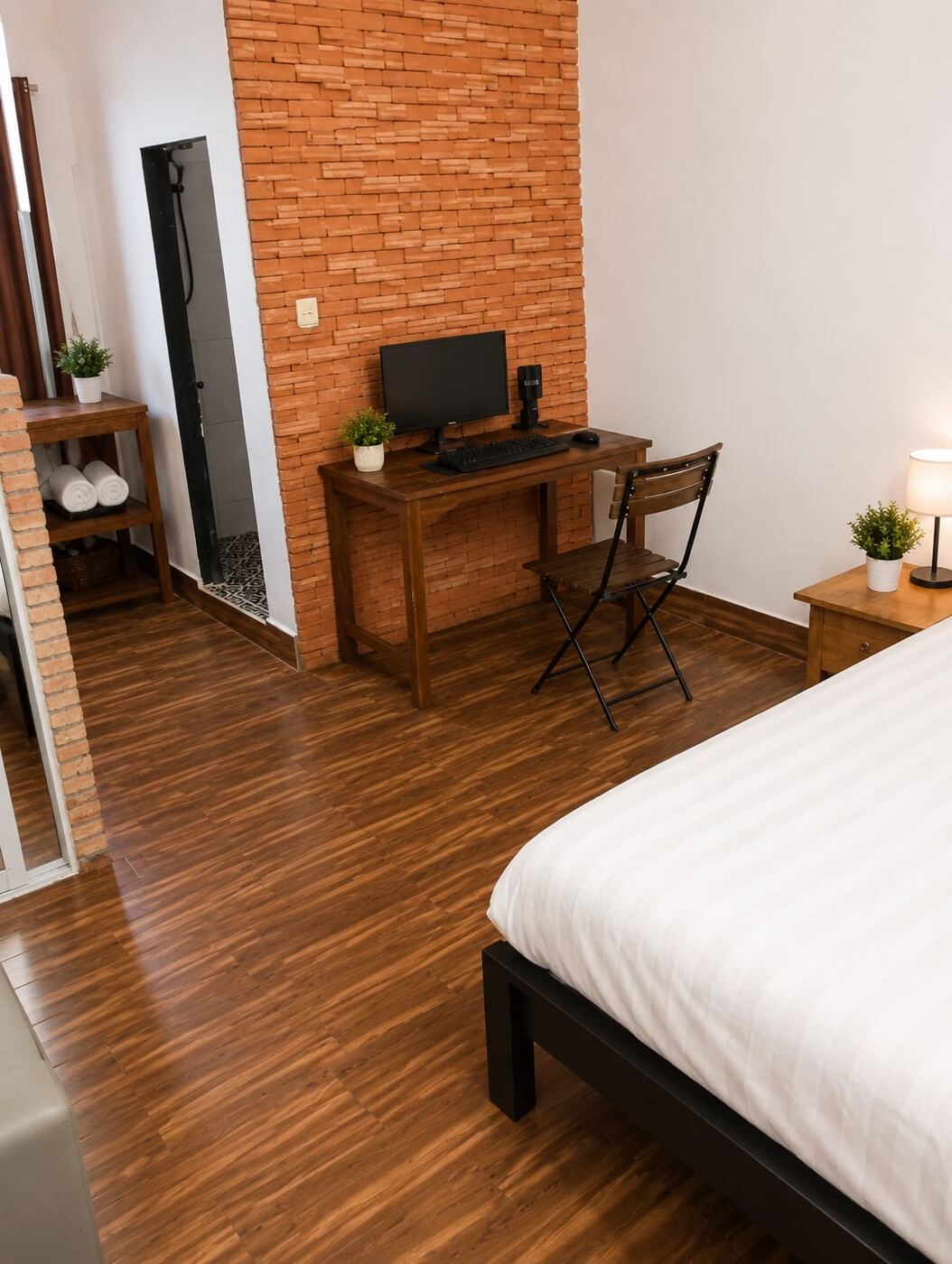 Studio interior with warm wood floor, exposed brick wall, work desk and double bed